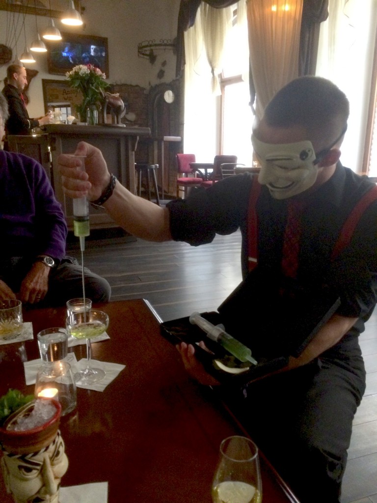 bartender wearing anonymous mask serves drink from needle